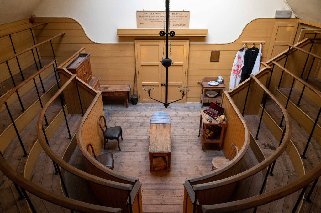 View from the top of the gallery old Victorian operating theatre, looking down over wooden seating and the operating table at the bottom centre.