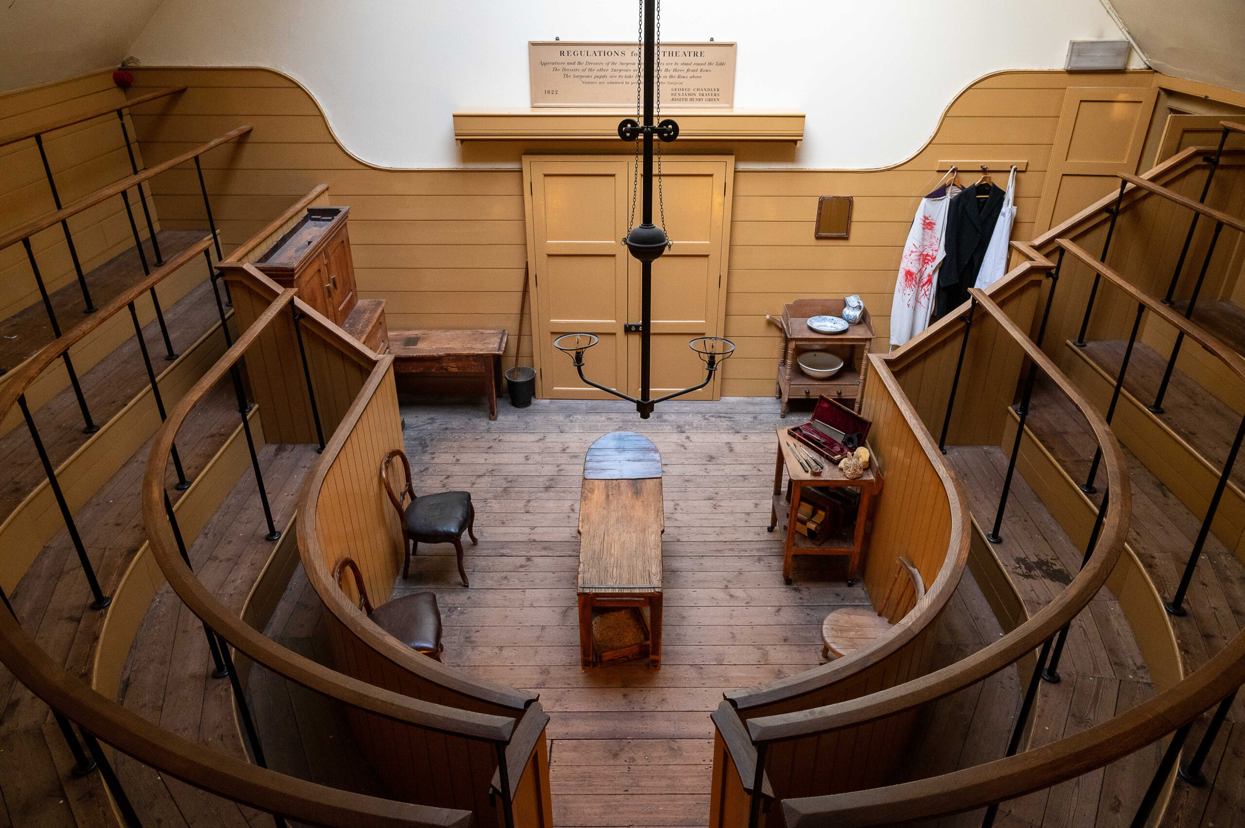 View from the top of the gallery old Victorian operating theatre, looking down over wooden seating and the operating table at the bottom centre.